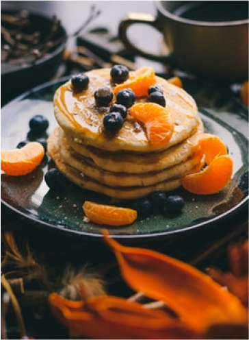 A stack of pancakes topped with blueberries and mandarine orange slices.