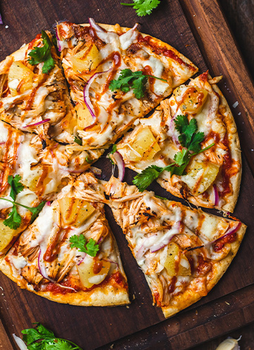 A pineapple bbq chicken pizza sitting on a cutting board.